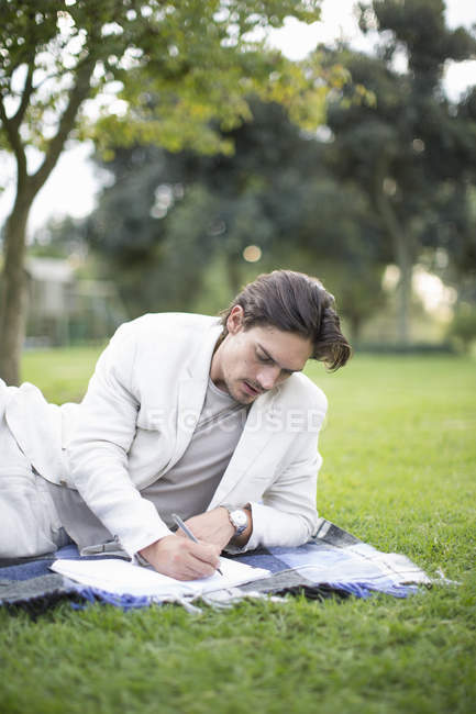 Geschäftsmann liegt auf Picknickdecke und schreibt Notizen im Park — Stockfoto