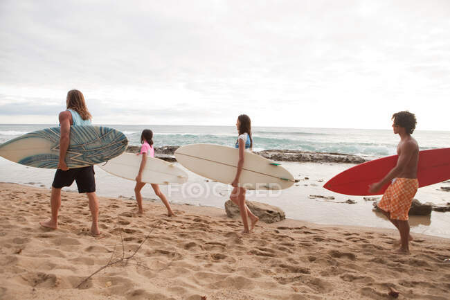 Quatre jeunes amis portant des planches de surf sur la plage — Photo de stock
