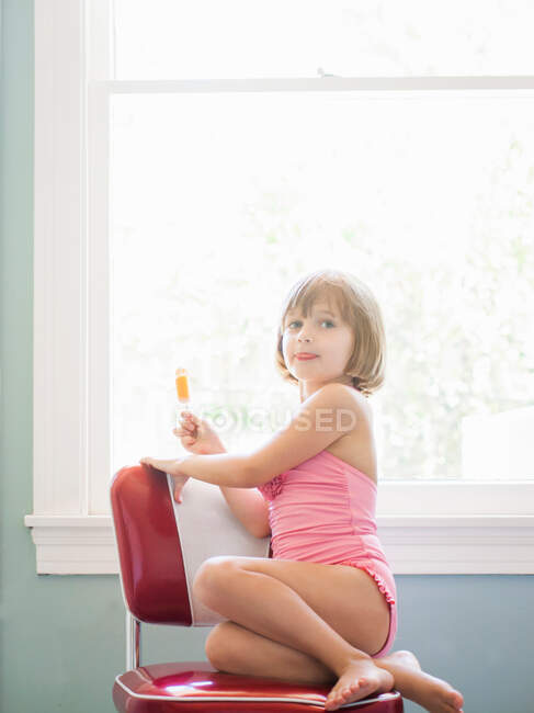 Menina sentada na cadeira vermelha segurando gelo alegre, retrato — Fotografia de Stock