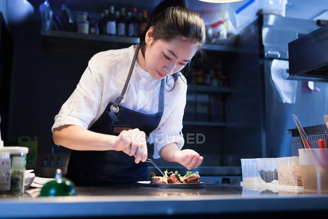 Chef in commercial kitchen seasoning food — Stock Photo