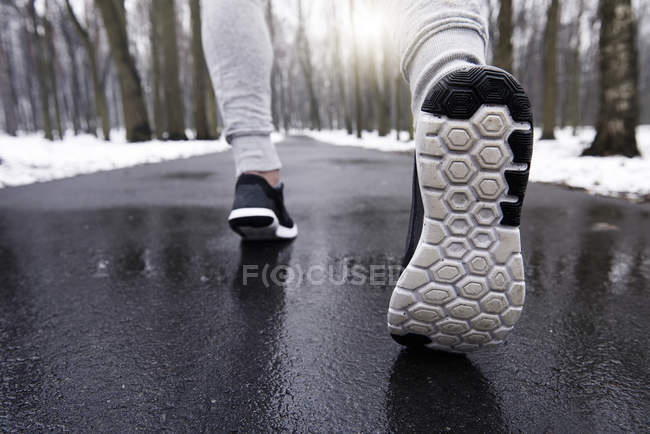 Young man jogging through snowy forest, low section, rear view — Stock Photo