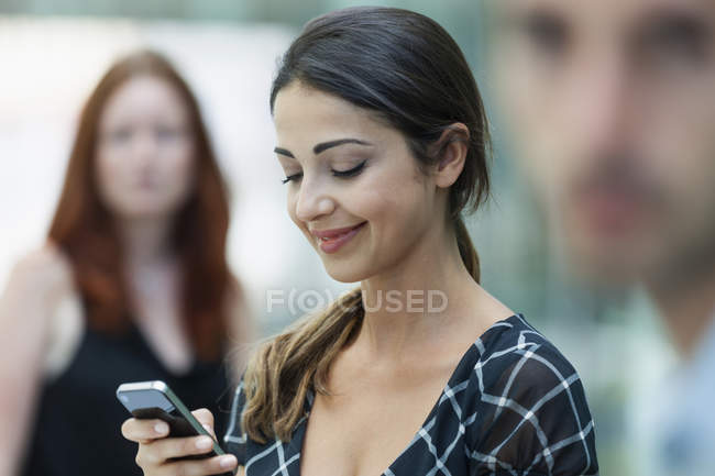 Femme utilisant le téléphone, collègues en arrière-plan — Photo de stock