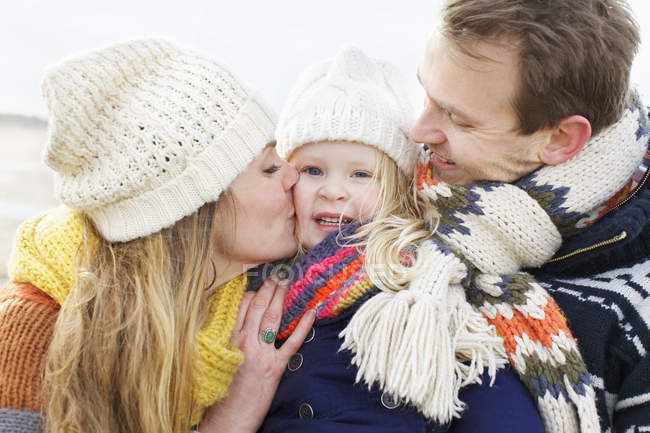 Metà genitori adulti baciare la figlia sulla guancia a costa — Foto stock