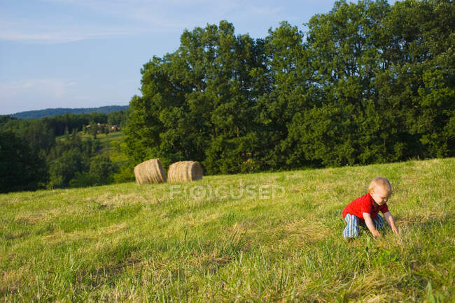 Un niño agachado en un campo - foto de stock