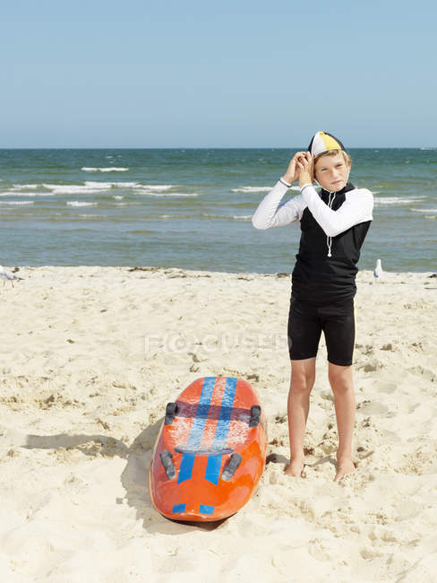 Retrato de niño nieto (niños salvavidas surf) poniéndose gorra, Altona, Melbourne, Australia - foto de stock