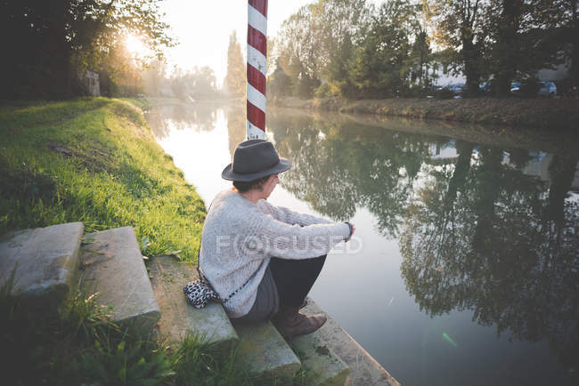 Young woman sitting on steps by river, Dolo, Venice, Italy — Stock Photo