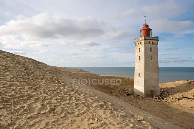 Lighthouse on sandy beach with cloudy sky at sunset — Stock Photo