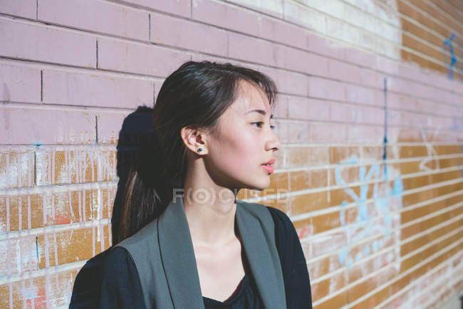 Portrait de jeune femme appuyée contre un mur de briques graffiti — Photo de stock