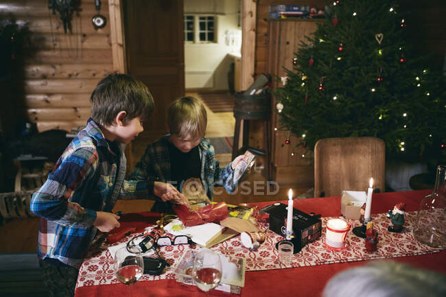 Due fratelli aprono i regali di Natale a tavola — Foto stock