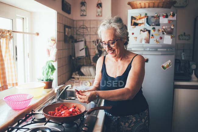 Woman chopping tomatoes into saucepan smiling — Stock Photo