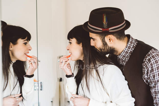 Young man with woman applying lipstick in front of mirror — Stock Photo