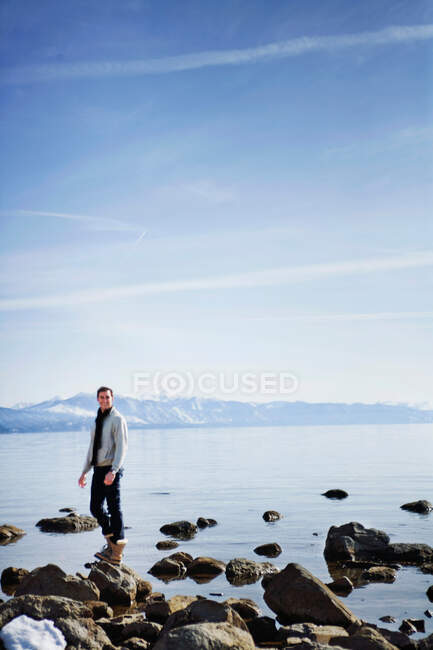 Uomo in piedi sulla roccia vicino al lago — Foto stock