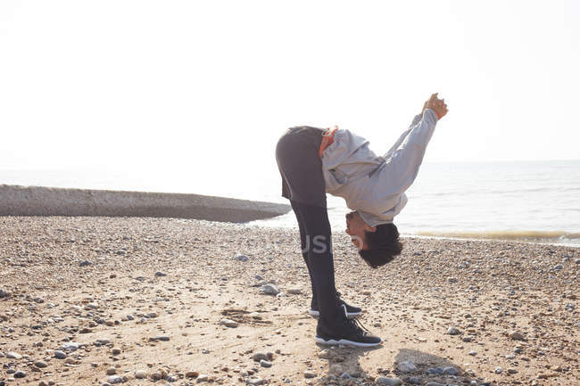 Hombre joven entrenando, inclinándose hacia adelante en la playa de Brighton - foto de stock