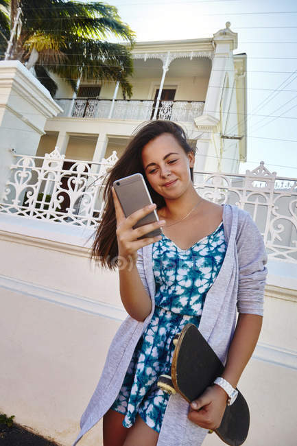 Giovane ragazza, all'aperto, portando skateboard, utilizzando smartphone — Foto stock