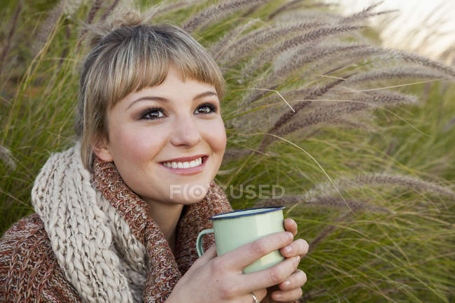 Portrait of young woman amongst long grass with drinks mug — Stock Photo