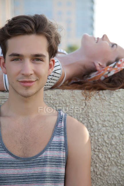 Young woman lying on wall with young man in front, portrait — Stock Photo