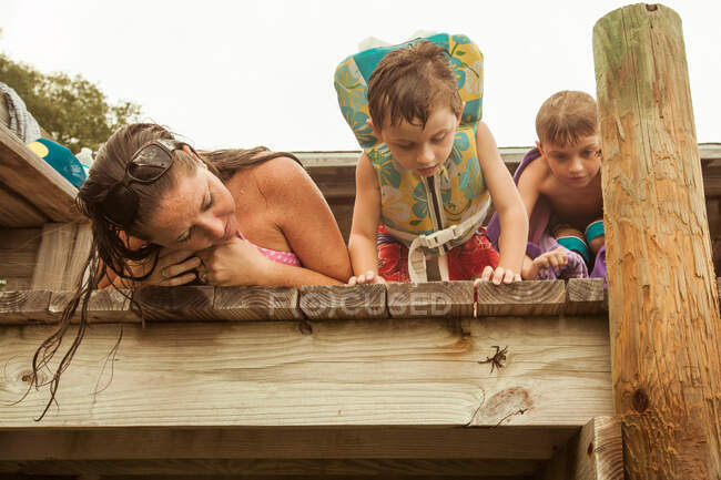 Mother with two sons peering over jetty looking at hermit crab — Stock Photo