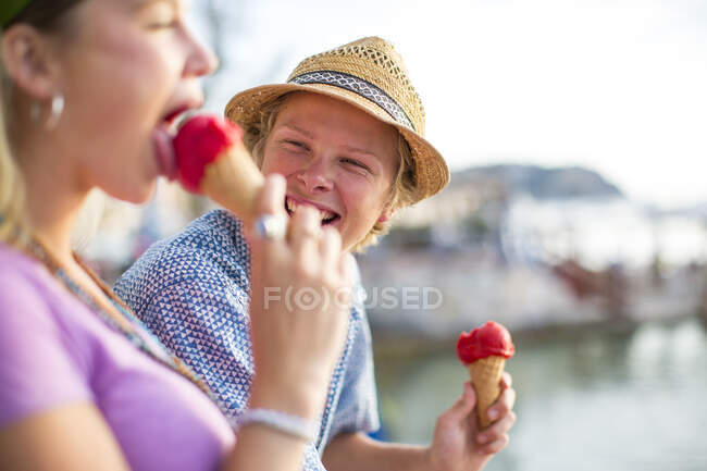 Casal jovem rindo e comendo cones de sorvete à beira-mar, Maiorca, Espanha — Fotografia de Stock