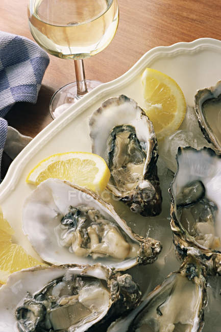 Dish of oysters with lemon slices and wine glass on table — Stock Photo