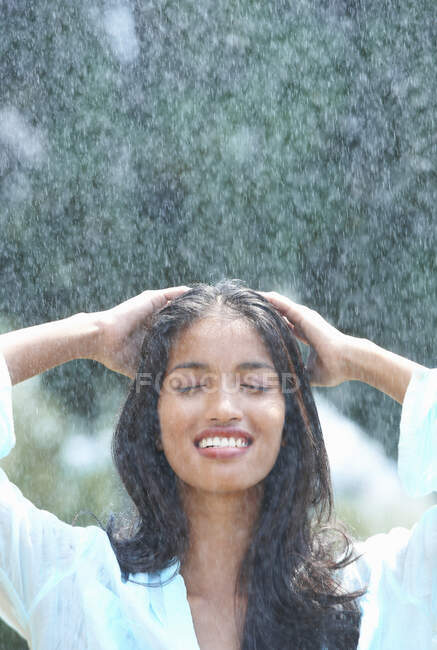 Молодая женщина моет волосы под дождем — стоковое фото