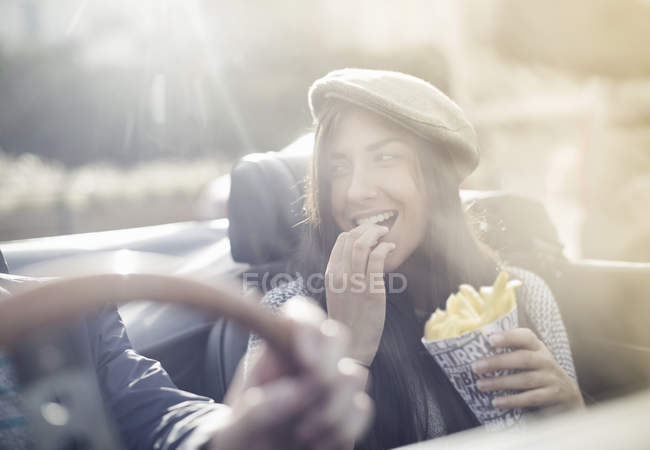 Jovem casal no conversível, mulher comer batatas fritas — Fotografia de Stock