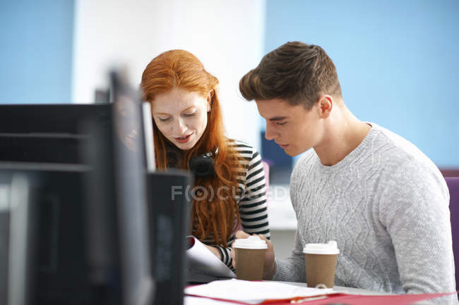 Jeunes étudiantes et étudiants masculins et féminins lisant au bureau informatique — Photo de stock