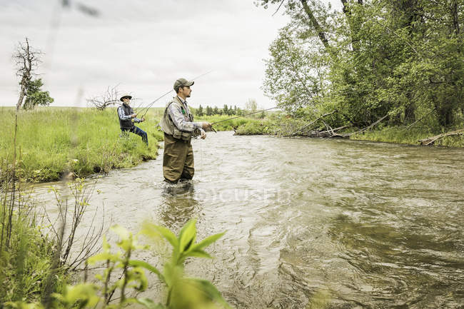 Homme portant des échassiers genoux profondément dans la pêche en eau dans la rivière — Photo de stock