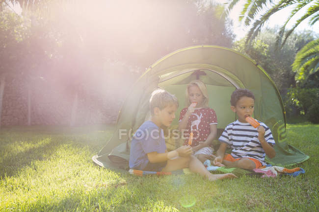 Trois enfants mangeant des sucettes de glace dans une tente de jardin — Photo de stock