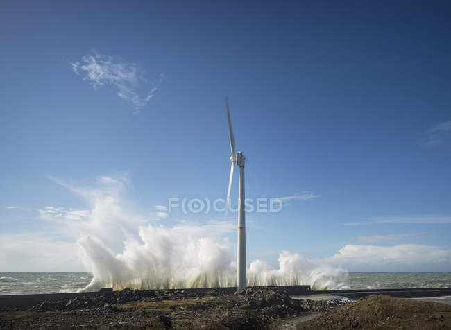 Turbina eolica con onde di tempesta sulla costa sotto il cielo blu — Foto stock