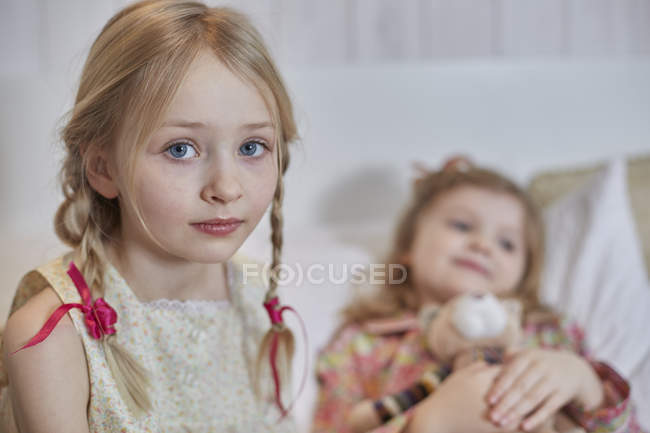 Girl with braided hair, sister hugging teddy bear in background — Stock Photo
