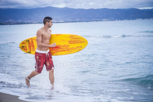 Junger männlicher Surfer läuft mit Surfbrett am Strand von Cagliari, Sardinien, Italien — Stockfoto