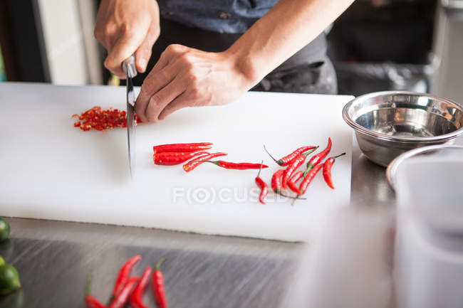 Imagen recortada de hombre rebanando chiles rojos - foto de stock