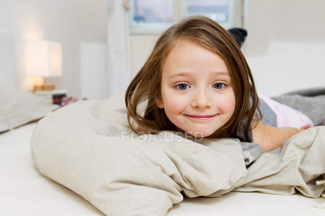 Усміхнена дівчина лежить на ліжку, фокус на передньому плані — стокове фото