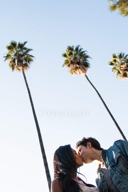 Young couple walking outdoors, kissing, low angle view — Stock Photo