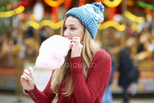 Giovane donna mangiare caramelle filo interdentale al luna park, all'aperto — Foto stock