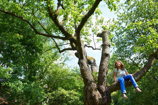 Улыбающаяся девочка, сидящая на дереве снаружи — стоковое фото