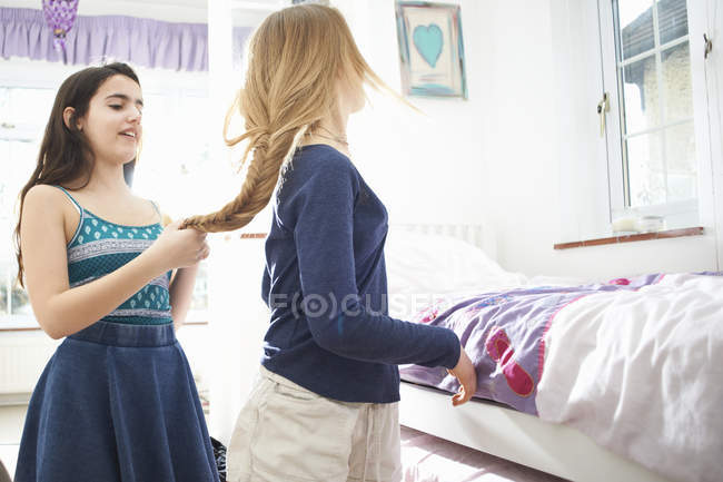 Adolescente chica trenzando mejores amigos pelo en el dormitorio - foto de stock