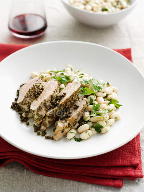 Plate of chicken with capers and beans served on table — Stock Photo