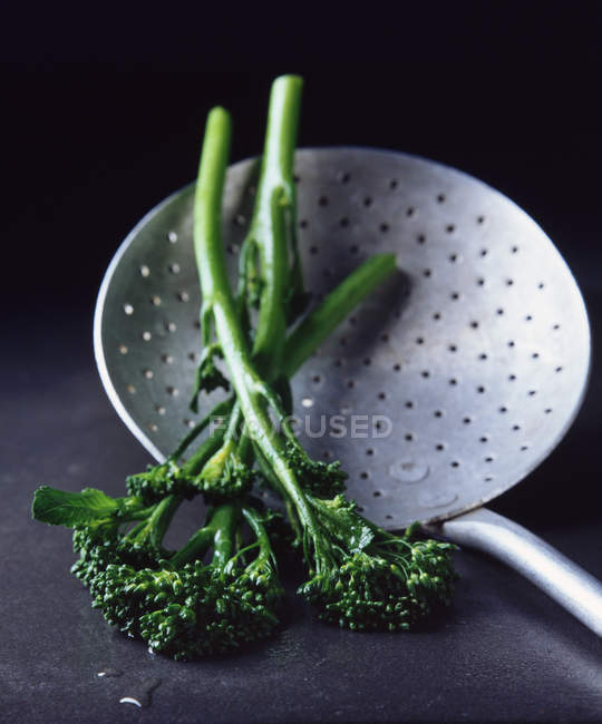 Primo piano colpo di broccolini bolliti su mestolo perforato — Foto stock