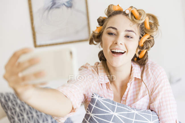Giovane donna con rulli in schiuma nei capelli, utilizzando lo smartphone, in videochiamata — Foto stock