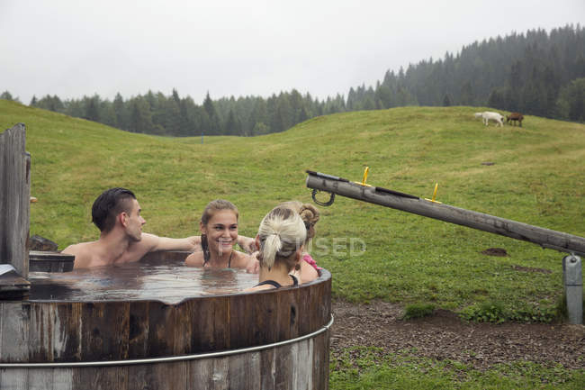 Quatro amigos adultos relaxando na banheira de hidromassagem rural, Sattelbergalm, Tirol, Áustria — Fotografia de Stock