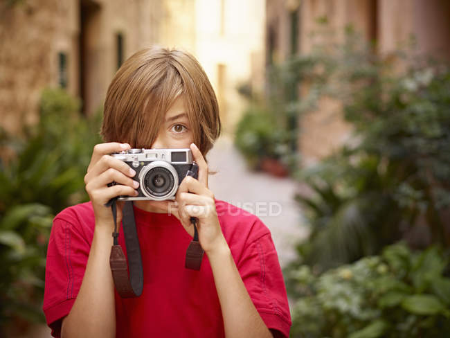 Retrato de niño fotografiando calle del pueblo con cámara SLR, Mallorca, España - foto de stock