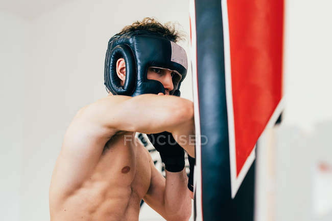 Homem usando protetor de cabeça sparring com saco de pancada — Fotografia de Stock