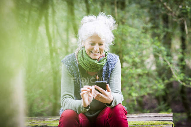 Зрелая женщина-садовница делает перерыв, глядя на смартфон — стоковое фото