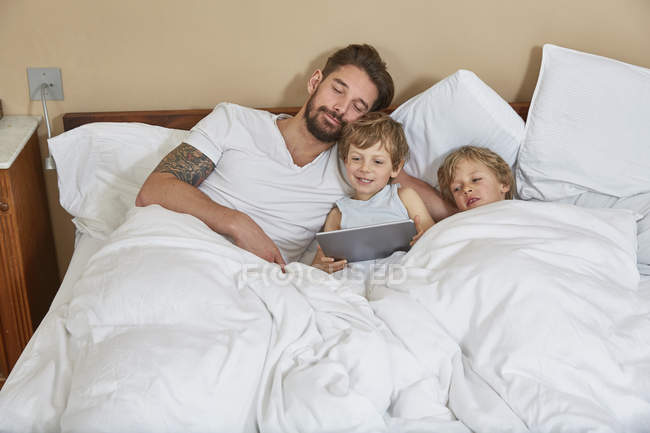 Отец и сыновья в постели с помощью цифрового планшета — стоковое фото