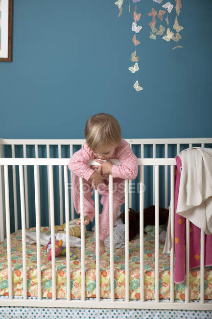 Female toddler climbing over side of crib — Stock Photo