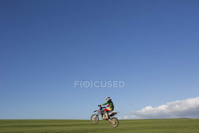 Joven corredor de motocross macho cabalgando a través del campo - foto de stock