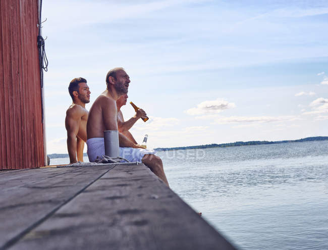 Tres amigos sentados afuera de la sauna disfrutando de la cerveza - foto de stock