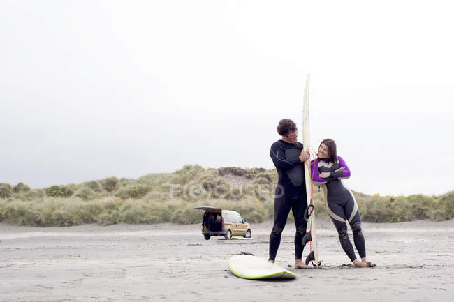 Couple on beach, woman leaning on surfboard — Stock Photo