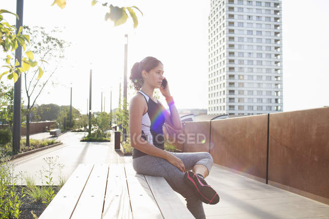 Woman training, sitting on urban footbridge talking on smartphone — Stock Photo